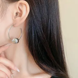 Close-up view of a large silver hoop earring with a polished metal bead on an Asian model.