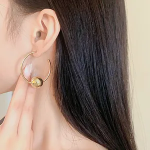 Close-up detail of minimalist gold hoop earrings with a polished bead on Asian model
