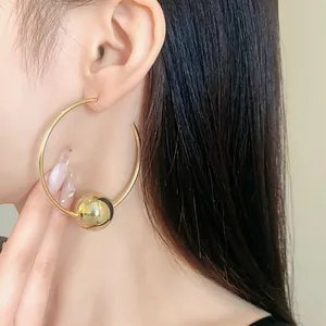 Close-up of minimalist gold hoop earrings with sliding bead on model, silver needles.