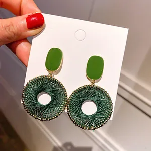 Detailed view of dark green woven round hoop earrings with enameled rectangular top
