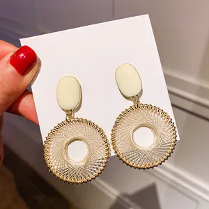 Close-up of woven circular earrings with beige enamel oval drop and gold metallic trim