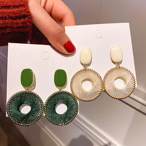 Close-up of woven round pendant earrings with drip oil rectangular tops in green and white.