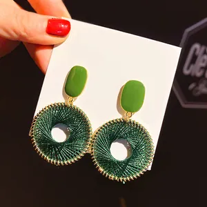 Detailed view of green enamel rectangle and dark green woven circular drop earrings.
