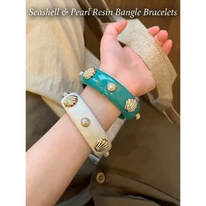 Bracciali rigidi vintage in resina con dettagli di conchiglie dorate e perle eleganti.