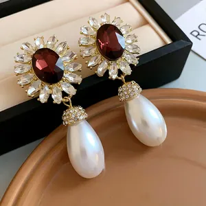 Gros plan de boucles d'oreilles fleurs de style français avec gemmes bordeaux et perles.