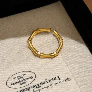 Macro detail of a brushed gold bamboo-inspired open ring with sparkling white zircons.