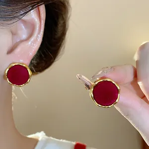 Detalle de pendientes redondos rojos flocados con bordes dorados y aguja plata