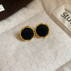 Detalle de pendientes de botón redondos de flocado negro con bordes dorados ondulados.