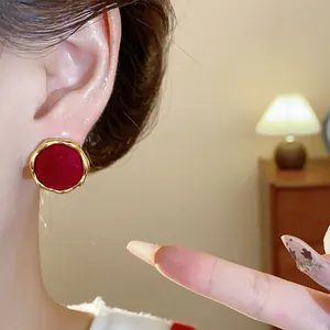 Primer plano de un pendiente redondo flocado rojo con elegante borde dorado ondulado en la oreja