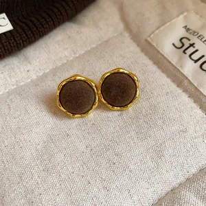 Detalle de pendientes redondos flocados con un borde dorado de diseño texturizado