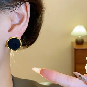 Primer plano de pendientes redondos flocados negros con borde dorado irregular