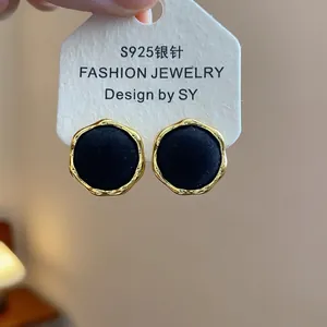 Detalle de pendientes redondos de flocado negro con borde dorado ondulado en tarjeta.