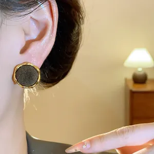 Elegantes pendientes dorados con flocado negro mostrados en la oreja de una modelo real