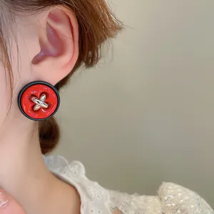 Gros plan d'une boucle d'oreille bouton rouge vintage avec coutures argentées sur un mannequin.
