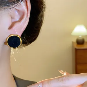 Primer plano de un elegante pendiente redondo flocado negro con borde dorado ondulado.