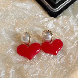 Gros plan de boucles d'oreilles cœur rouge élégantes avec perles sur fond texturé.