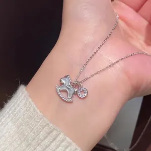 Gros plan d'un collier cheval à bascule avec zircons sur une manche de pull doux.