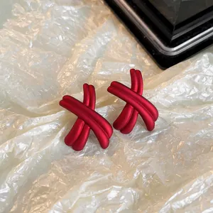 Vue détaillée de boucles d'oreilles rouges mates en forme de X sur papier blanc gaufré