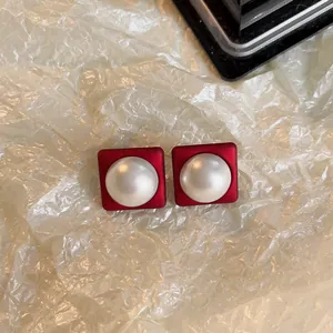 Gros plan de boucles d'oreilles carrées rouges avec une grande perle blanche au centre.