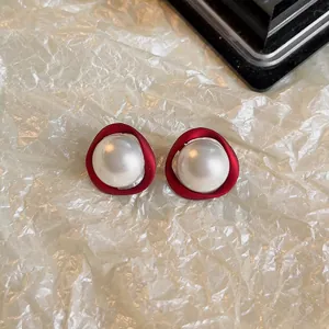Gros plan de boucles d'oreilles rétro rouges avec perle blanche sur fond texturé.