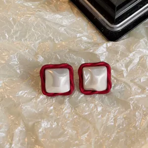 Détail de boucles d'oreilles carrées rouges rétro avec centre nacré sur papier