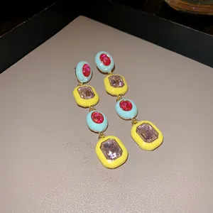 Detailansicht von bunten Emaille-Ohrhängern mit funkelnden facettierten Edelsteinen.