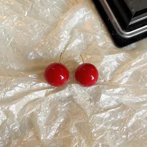 Vue détaillée de boucles d'oreilles boules rouges brillantes sur papier texturé blanc