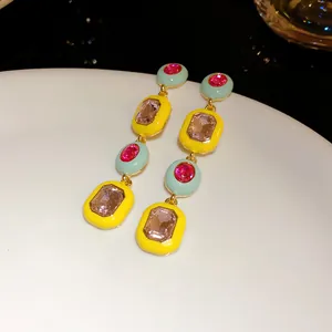 Detail von geometrischen Ohrhängern mit gelber Emaille und pinkfarbenen Kristallen