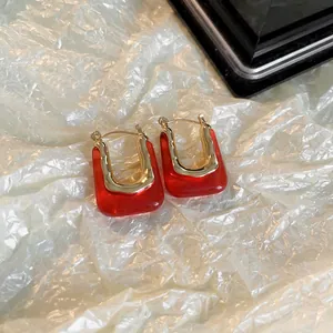 Vue détaillée de boucles d'oreilles carrées en résine rouge avec accents dorés