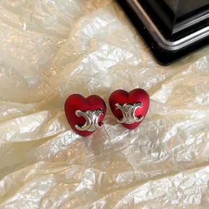 Vue détaillée de boucles d'oreilles cœur rouge avec logo Triomphe argenté et aiguille.
