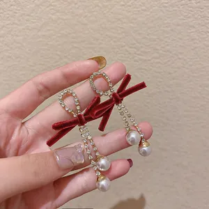 Gros plan de boucles d'oreilles nœud en velours rouge avec glands en strass et perles.
