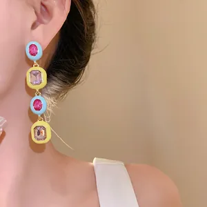 Nahaufnahme von geometrischen Ohrringen mit buntem Emaille-Dekor und Kristallen am Ohr