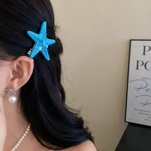Close-up of a blue starfish hair clip worn on black hair with pearl jewelry
