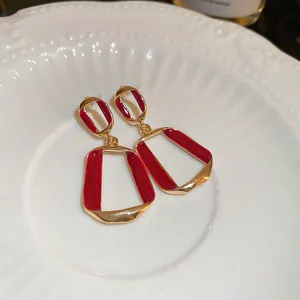 Vue détaillée de boucles d'oreilles géométriques en émail rouge avec monture dorée sur plat.