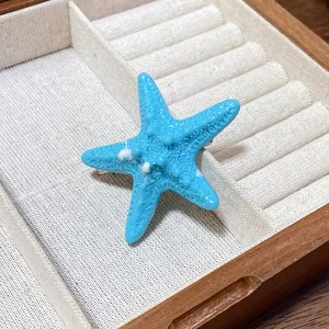 Detail shot of a vibrant blue acrylic starfish hair clip resting in a wooden jewelry box.