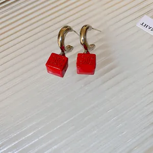 Gros plan sur des créoles argentées avec pendentifs cubes rouges et motif Triomphe.