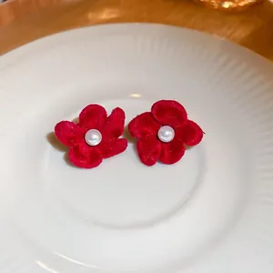 Gros plan sur les boucles d'oreilles fleur en velours rouge avec centre perle