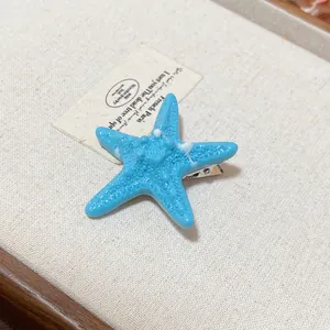 Detailed macro view of a blue starfish hair clip resting on a vintage beige tray.