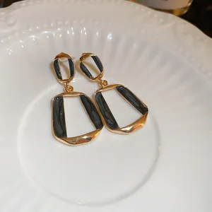 Détail rapproché d'élégantes boucles d'oreilles géométriques dorées avec émail noir texturé