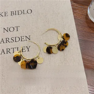 Close-up detail of stylish tortoiseshell and gold tassel hoop earrings on linen cloth