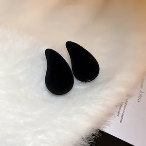 Gros plan de boucles d'oreilles clous noires en forme de larme sur fausse fourrure blanche