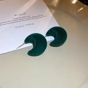 Vue macro de boucles d'oreilles croissants en velours vert foncé sur carte.
