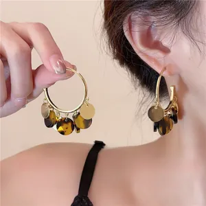 Detail shot showing gold-plated hoop earrings with dark tortoiseshell coin tassel drops