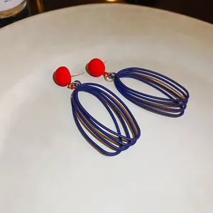 Gros plan sur des boucles d'oreilles boule rouge et fils bleus entrelacés