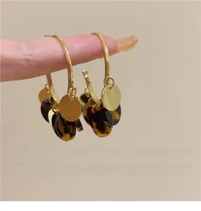 Elegant gold hoop earrings featuring dark tortoiseshell and round gold charms detail
