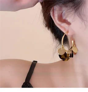Close-up of elegant gold hoop earrings with dark tortoiseshell and gold disc charms