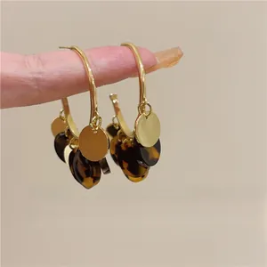 Close-up detail of tortoiseshell and golden disc charms hanging from stylish hoop earrings.