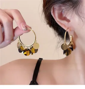 Close-up of S925 silver needle hoop earrings with dark tortoiseshell tassels and gold discs