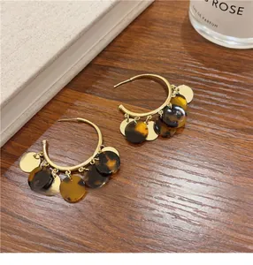 Close-up of elegant dark tortoiseshell tassel hoop earrings on a wooden background