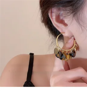 Close-up of gold hoop earrings with tortoise shell tassel pendants worn by model